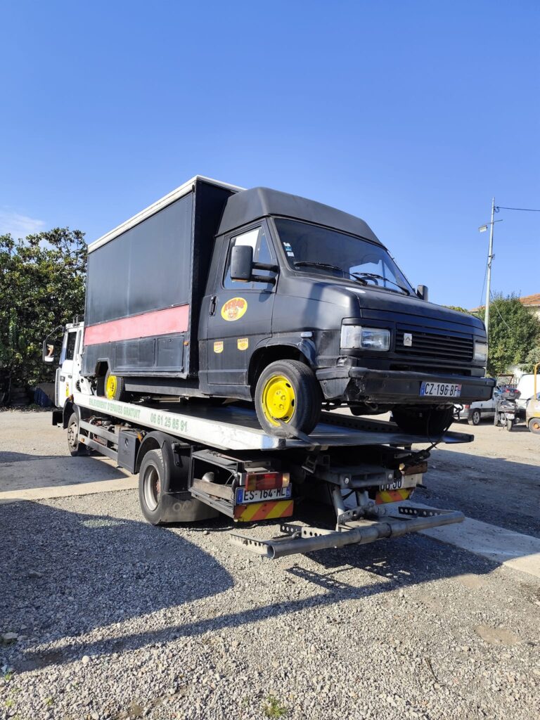 Dépanneuse : Enlèvement d’épave gratuit d’utilitaire Kebab. Dépanneuse transportant un utilitaire noir Kebab aux jantes jaunes. Texte: "ENLÈVEMENT D'ÉPAVES GRATUIT 06 61 25 85 91".